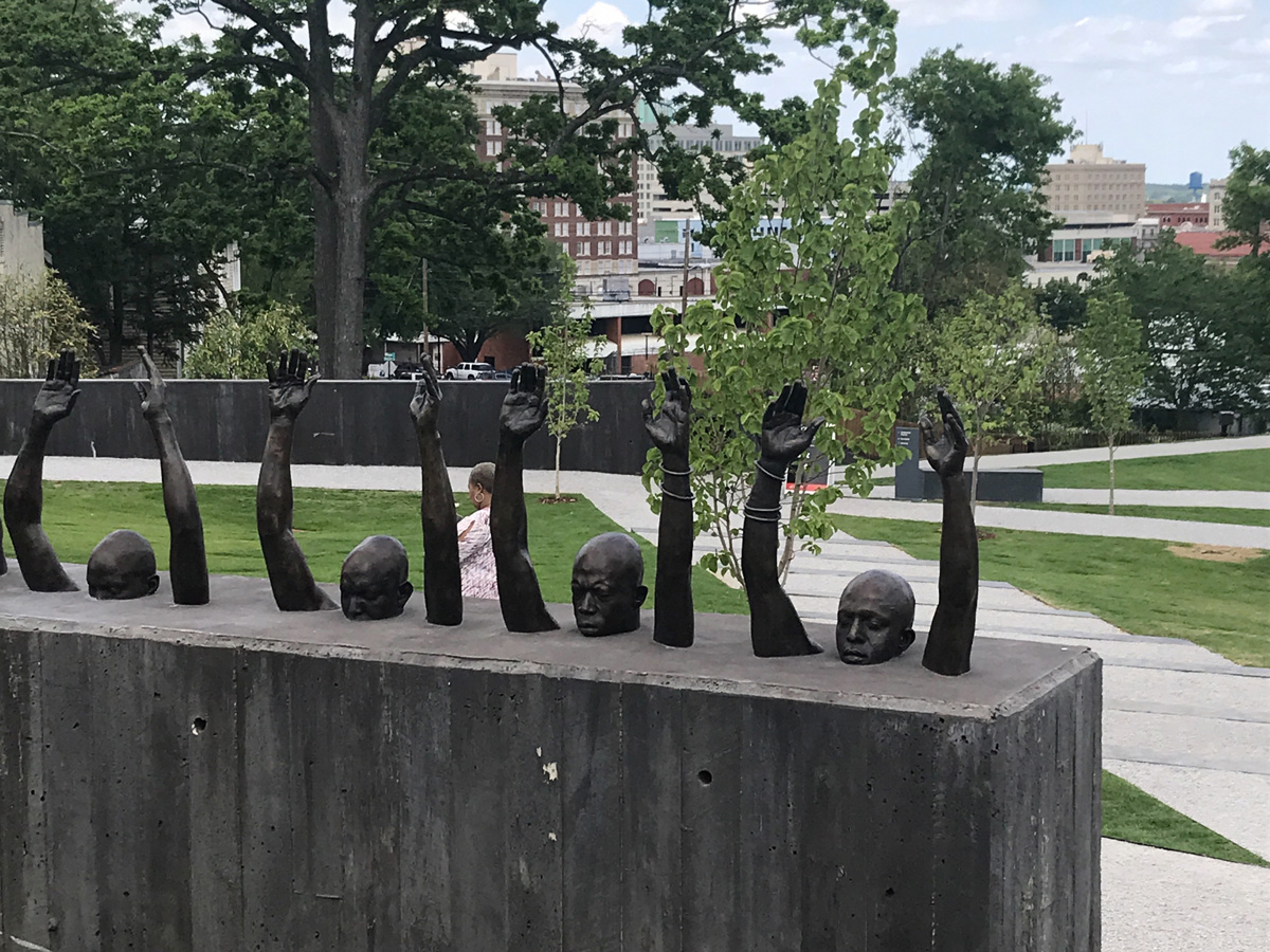 Sculpture of people with arms raised rising from wall of concrete.