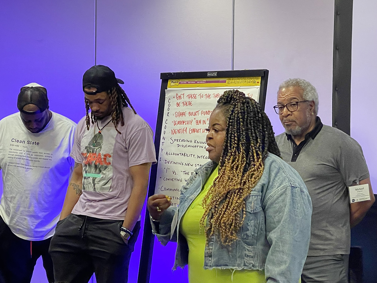 A person speaking with a large drawing pad and three people behind them.