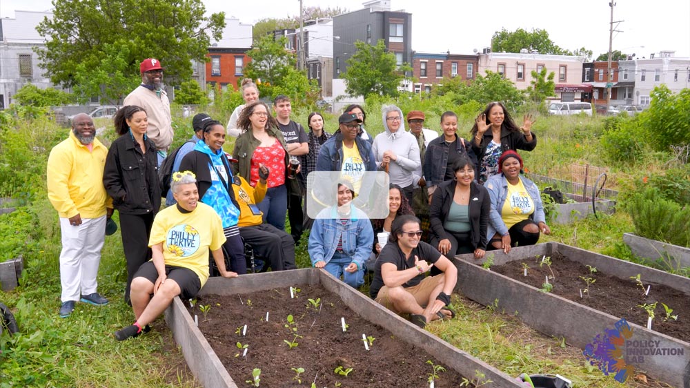 Play Video. Group of smiling people outside near garden beds with small plant sprouts.