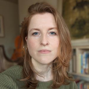 Headshot of a white woman with shoulder length red hair, wearing a green sweater. 