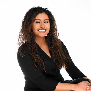 Photo of Anya Dickson-Arguello, Latina with long hair wearing a black dress and seated angling towards the right.